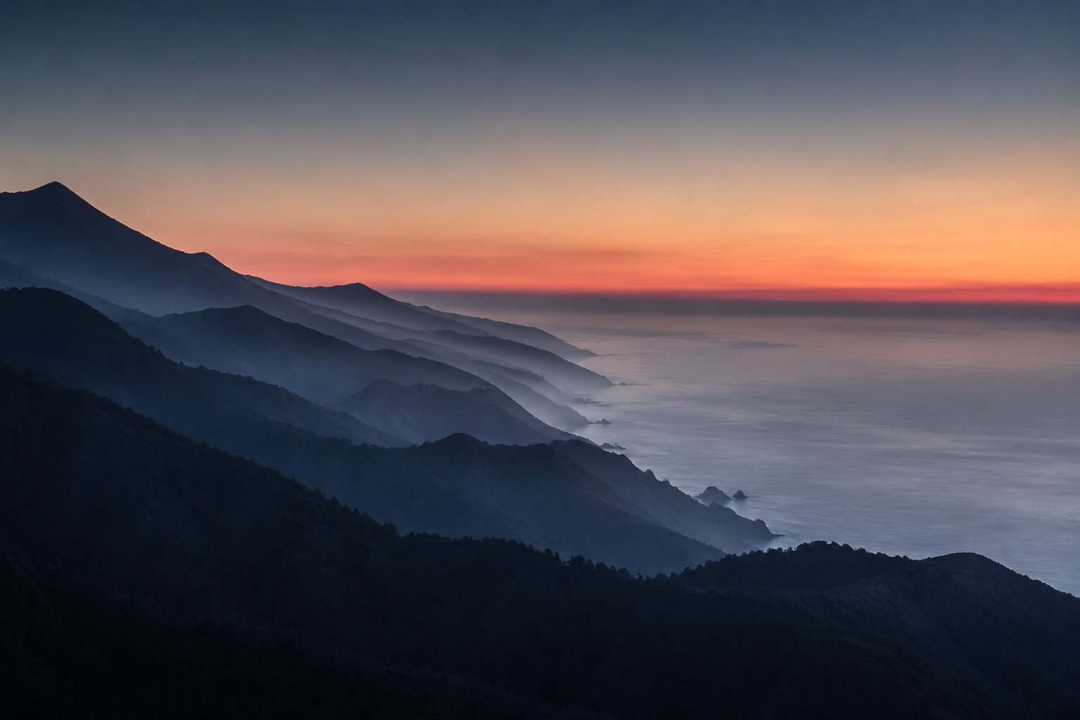 Layered coastal ridges descending toward a misty ocean at dawn